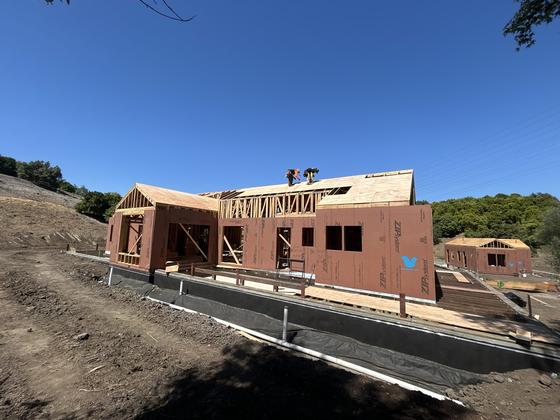 Large custom home fully framed and sheathed on a hillside site with crew on the roof