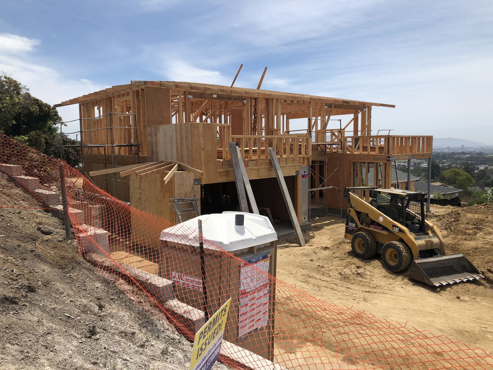 Two-story custom home framed on a hillside lot with skid steer out front and city views